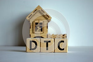 Wooden cubes form the word `DTC` near miniature house. Beautiful white background, copy space. Home delivery concept