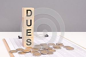 wooden cubes forming the text Dues, surrounded by coins, symbolize a commitment to financial obligations and membership