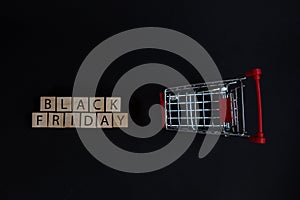 Wooden cubes with the inscription-Black Friday on a black background with a shopping basket, sales concept, business management