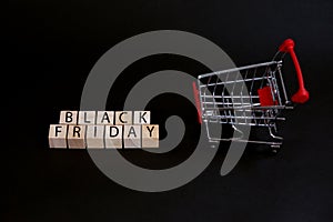 Wooden cubes with the inscription-Black Friday on a black background with a shopping basket, sales concept, business management
