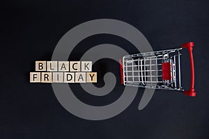 Wooden cubes with the inscription-black Friday on a black background with a supermarket shopping cart