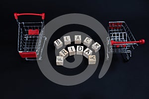 Wooden cubes with the inscription-black Friday between two supermarket shopping carts