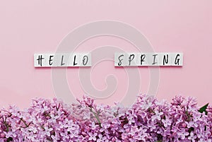 wooden cubes with the inscription hello spring, lilac branches on a pink background, seasonal concept