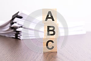 wooden cubes with letters ABC arranged in a vertical pyramid, stack white paper on background, business concept, ABC -