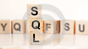 wooden cubes with letters SQL arranged in a vertical pyramid, white background, reflection from the surface of the table