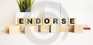 Wooden cubes with letters on a white table. The word is ENDORSE. White background photo