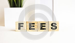 Wooden cubes with letters on a white table. The word is FEES. White background