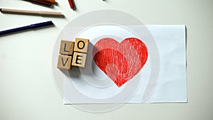 Wooden cubes with love word lying on red heart picture, true relationships