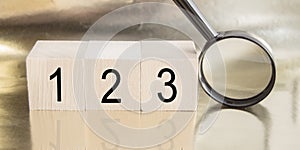 Wooden cubes with numbers 1,2,3 and magnifying glass on golden background with reflection, BASIC BUSINESS concept