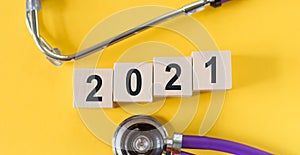 Wooden cubes with numbers 2021 and a stethoscope on a yellow background. Medical expectation 2021 concept
