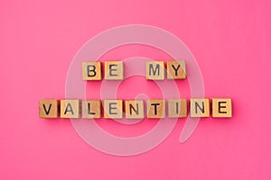 Wooden cubes with the phrase Be My Valentine on an empty colorful pink background. Words of love are made of letters