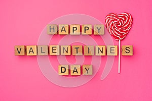 Wooden cubes with the phrase Happy Valentine`s Day on an empty colorful pink background. Words of love are made of letters from