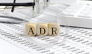 Wooden cubes with the word ADR on a financial background with chart, calculator, pen and glasses, business concept