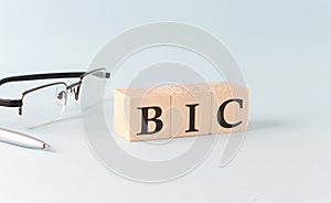 Wooden cubes with the word BIC Bank Identifier Code on financial background with chart, calculator, pen and glasses, business