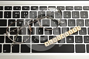 Wooden cubes with word Blacklist and glasses on laptop keyboard, top view