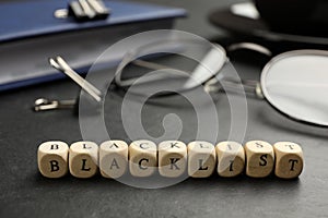 Wooden cubes with word Blacklist and office stationery on black desk, closeup