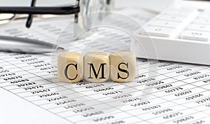 Wooden cubes with the word CMS stand on a financial background with chart, calculator, pen and glasses, business concept