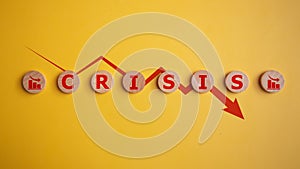 Wooden cubes with the word crisis and a red arrow down on a yellow background, business financial loss, crisis concept