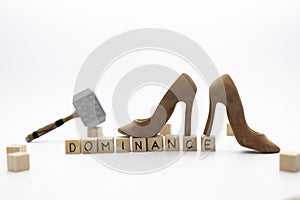The wooden cubes with the word DOMINANCE against white background with hammer and fashion wooden shoes is standing on cubes