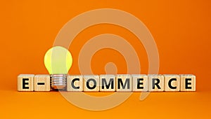 Wooden cubes with word `e-commerce`. Yellow light bulb. Beautiful orange background. Business concept. Copy space