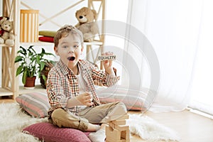 Wooden cubes with word EQUALITY in hands of little boy