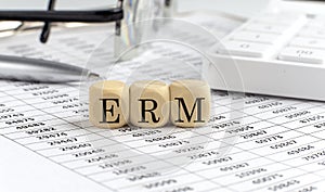 Wooden cubes with the word ERM on a financial background with chart, calculator, pen and glasses, business concept