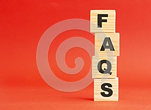 Wooden cubes with word FAQS. Wooden cubes on a red background. Free space on the left.