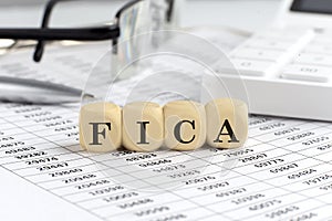 wooden cubes with the word FICA on a financial background with chart, calculator, pen and glasses, business concept