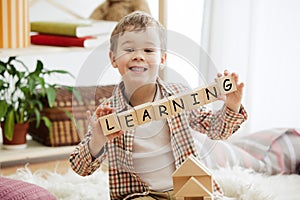 Wooden cubes with word LEARNING in hands of little boy