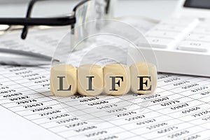 wooden cubes with the word LIFE on a financial background with chart, calculator, pen and glasses, business concept