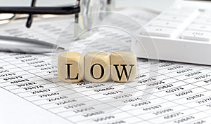 Wooden cubes with the word LOW on a financial background with chart, calculator, pen and glasses, business concept