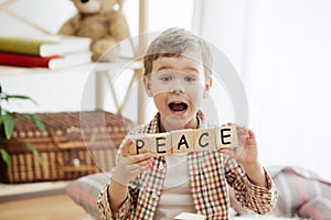 Wooden cubes with word PEACE in hands of little boy