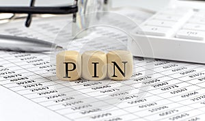 Wooden cubes with the word PIN on a financial background with chart, calculator, pen and glasses, business concept