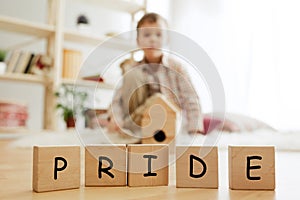 Wooden cubes with word PRIDE in hands of little boy