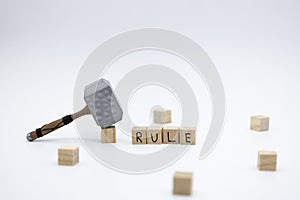 The wooden cubes with the word RULE and the weapon around against white background. The medieval hammer on a wooden cube