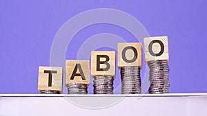 wooden cubes with the word Taboo on money pile of coins, business concept