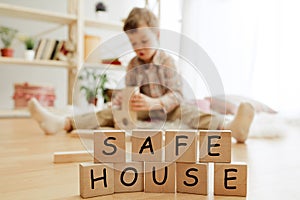 Wooden cubes with words SAFE HOUSE in hands of little boy