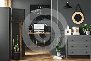 Wooden cupboard with decor, fresh plant and books standing in the real photo of open space living room interior with wainscoting