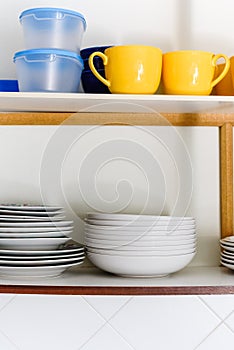 Wooden cupboard with piles of ceramic plates, cups and plastic containers