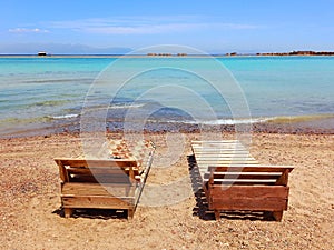 Wooden and cushion sun loungers and turquoise waters of the Red Sea on the Sinai Peninsula. Back view of empty sun loungers. Chill