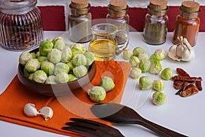 Wooden cutlery, various spices and butter near ripe brussels sprouts lies in a wooden bowl and on a table