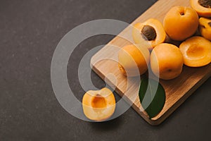 Wooden cutting board on black background with apricot halves and whote fruits. Fresh summer still life