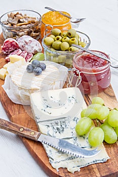 Wooden cutting board with cheese, cold cuts and jams