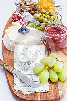 Wooden cutting board with cheese, cold cuts and jams