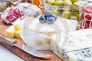 Wooden cutting board with cheese, cold cuts and jams