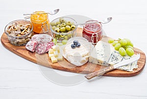 Wooden cutting board with cheese, cold cuts and jams