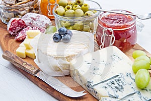 Wooden cutting board with cheese, cold cuts and jams