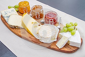 Wooden cutting board with cheese and jams