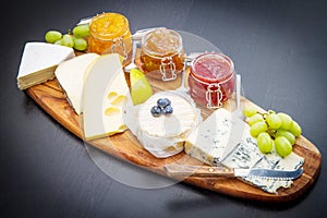 Wooden cutting board with cheese and jams