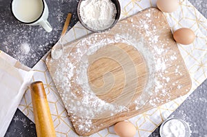 Wooden cutting board dusting with flour for dough.Empty round spot for text on the cutting board.Kitchen table and flour,eggs,salt